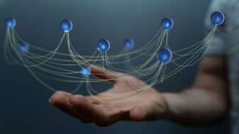 A hand supporting a network of interconnected blue nodes with glowing centers. Thin lines connect the nodes, symbolizing data flow and digital connectivity, representing the concept of 6G-powered IoT networks.
