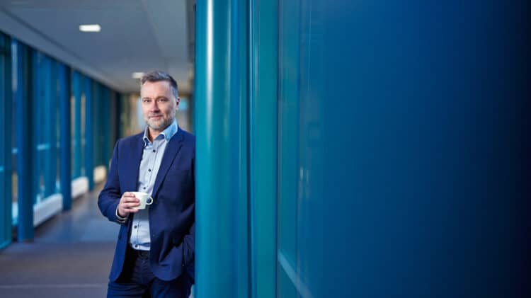 Research Director Hannu Nikurautio holding a coffee cup in a corridor at the University of Oulu.