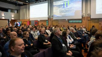 Audience at the Nordic Conference on Digital Health and Wireless Solutions attentively listening to a presentation, with the event agenda displayed on the screen.