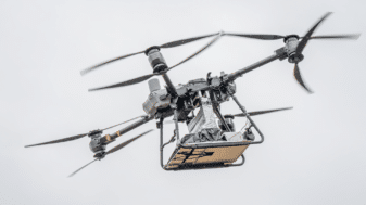 A large industrial drone in flight carrying a compact 5G base station payload, tested at Oulu Zone in Oulu, Finland, as part of a joint University of Oulu and University of Tokyo emergency communications research project.