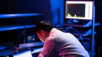 Scientist analysing data on multiple monitors in a dark lab.