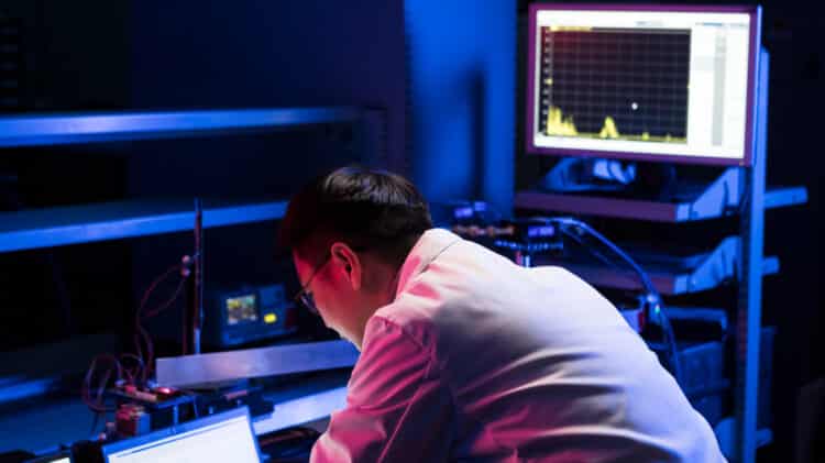 Scientist analysing data on multiple monitors in a dark lab.
