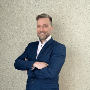 Hannu Nikurautio, Research Director of Defence at 6G Flagship, is in a navy blazer with arms crossed against a textured light grey background.