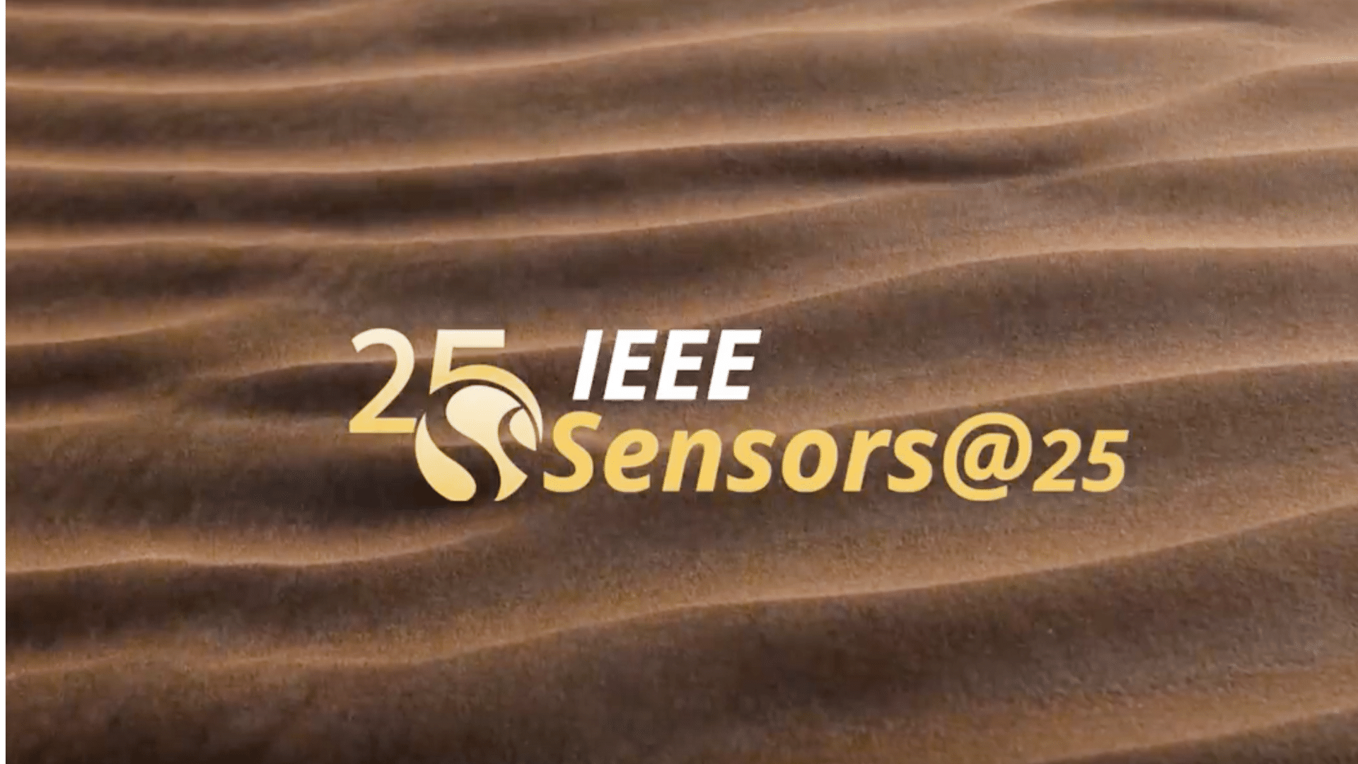 The IEEE Sensors@25 logo in gold and white over rippled desert sand.