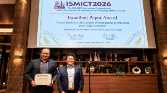 Erkki Harjula (on the left) holding the Excellent Paper Award certificate at ISMICT 2026 in Osaka, with the award slide on screen behind him.