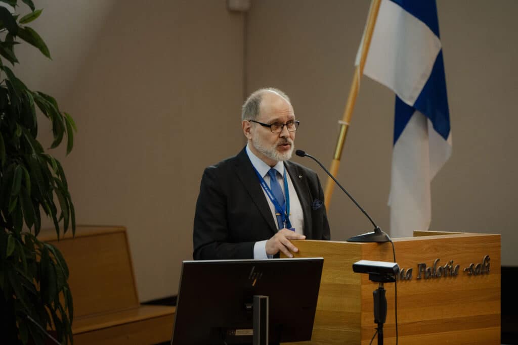 Jarmo Reponen speaking at a lectern beside the Finnish flag
