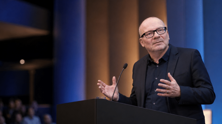 Seppo Yrjölä speaking at a conference podium during a corporate presentation. AI-assisted image.