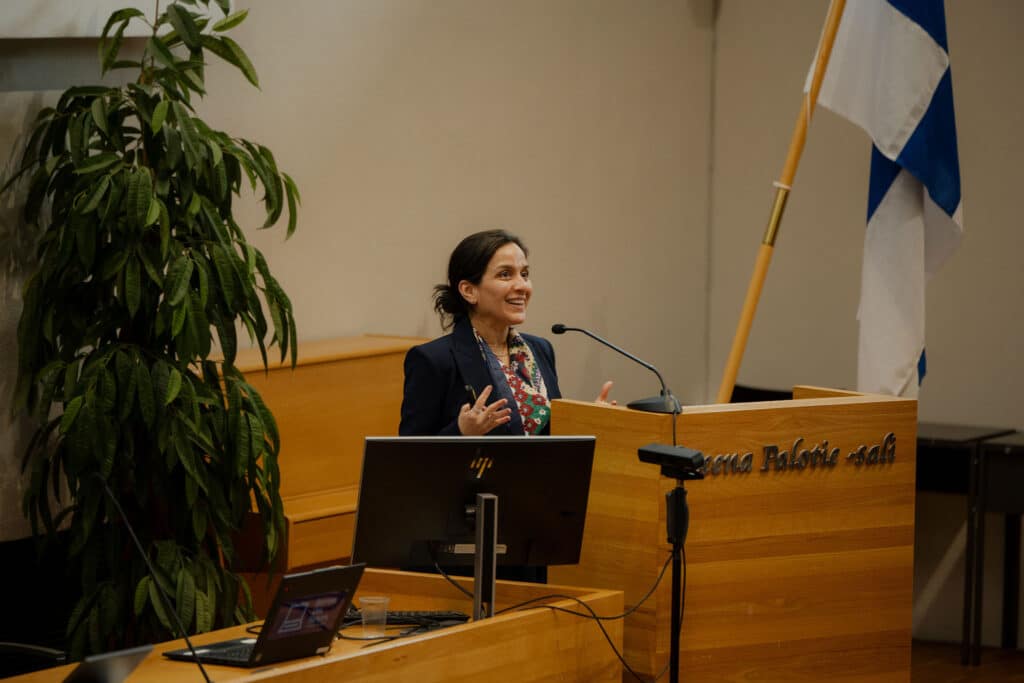 Smisha Agarwal giving the closing plenary keynote at a lectern beside the Finnish flag