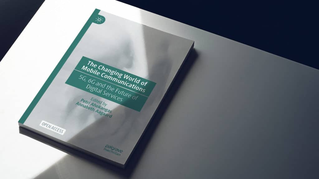A book titled "The Changing World of Mobile Communications: 5G and the Future of Digital Services" lies on a table with a focused light source casting shadows on its surface. The cover indicates it is an open access publication and lists Petri Ahokangas and Annabeth Aagaard as editors.